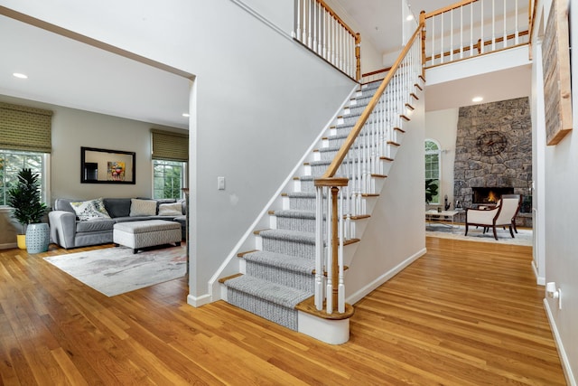 staircase featuring a fireplace, recessed lighting, a high ceiling, baseboards, and hardwood / wood-style flooring