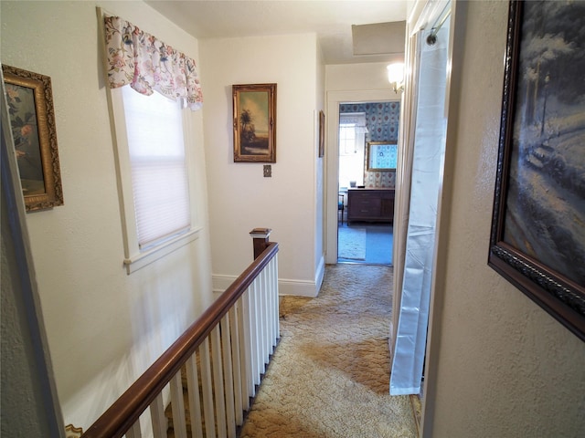 hall with baseboards, plenty of natural light, an upstairs landing, and light colored carpet