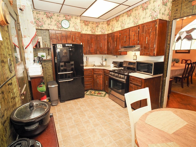 kitchen with a toaster, under cabinet range hood, stainless steel appliances, light countertops, and wallpapered walls