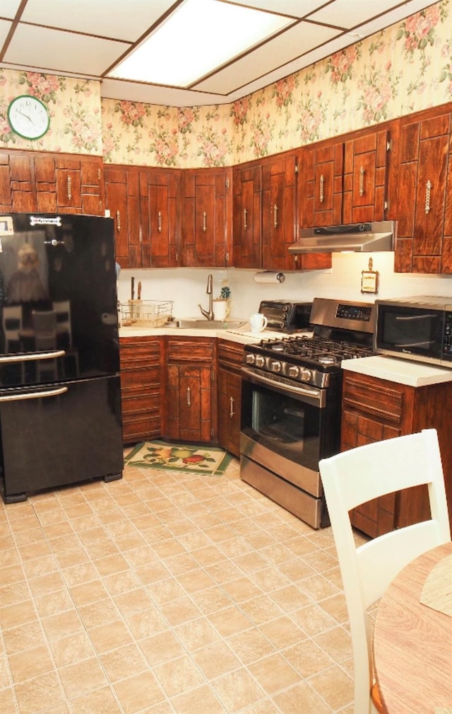 kitchen with stainless steel range with gas stovetop, freestanding refrigerator, under cabinet range hood, and wallpapered walls