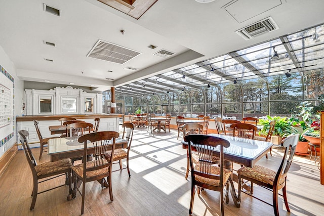 dining space with a sunroom, visible vents, and light wood-style floors