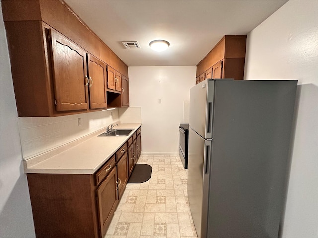 kitchen with light countertops, visible vents, electric range oven, freestanding refrigerator, and a sink