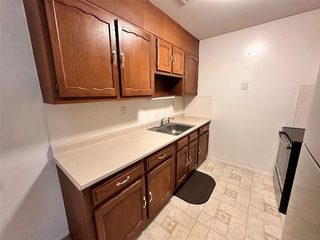 kitchen featuring a sink, baseboards, light countertops, backsplash, and stone finish floor