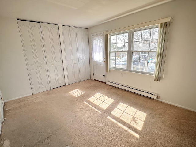 unfurnished bedroom featuring a baseboard heating unit, two closets, and baseboards