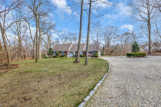 view of front of house with gravel driveway, a chimney, and a front lawn