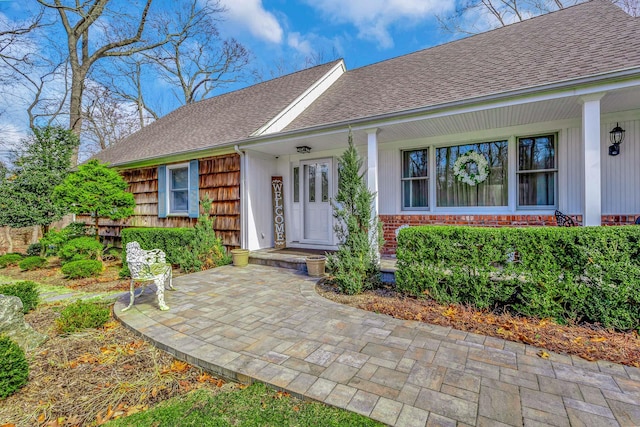 view of exterior entry with a shingled roof and brick siding