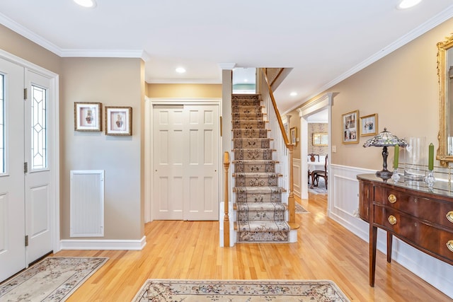 foyer entrance featuring crown molding, light wood-style floors, stairs, wainscoting, and ornate columns