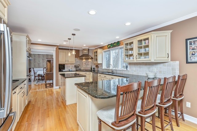 kitchen featuring light wood finished floors, tasteful backsplash, wall chimney exhaust hood, a center island, and a peninsula