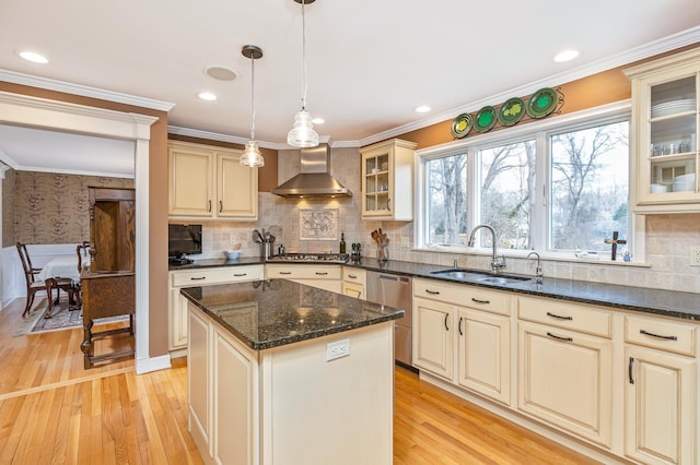 kitchen with wall chimney range hood, cream cabinets, and a sink