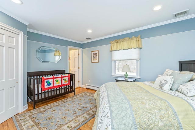 bedroom with visible vents, a baseboard heating unit, wood finished floors, and ornamental molding