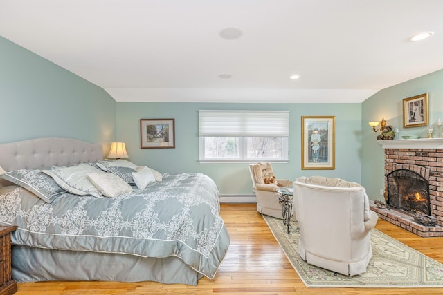 bedroom featuring a brick fireplace, a baseboard radiator, light wood finished floors, and recessed lighting