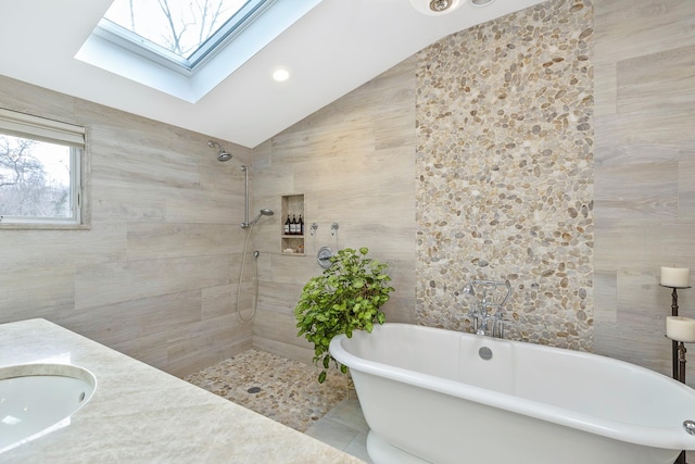 full bath with tile walls, lofted ceiling with skylight, a soaking tub, a tile shower, and a sink