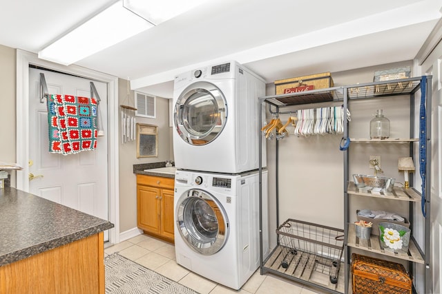 washroom featuring light tile patterned floors, stacked washer and dryer, cabinet space, and visible vents