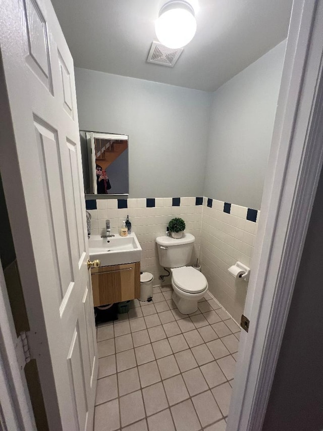 bathroom with toilet, vanity, visible vents, tile walls, and tile patterned floors