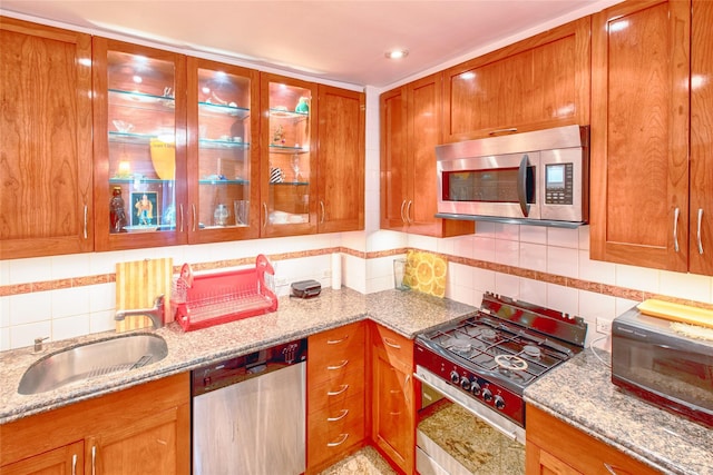 kitchen with light stone counters, tasteful backsplash, appliances with stainless steel finishes, glass insert cabinets, and a sink