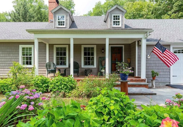 view of front of property featuring an attached garage, covered porch, a chimney, and roof with shingles