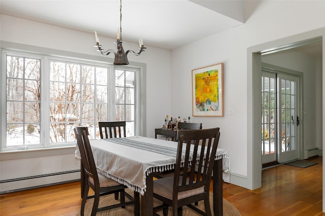 dining room featuring a chandelier, a wealth of natural light, baseboard heating, and wood finished floors