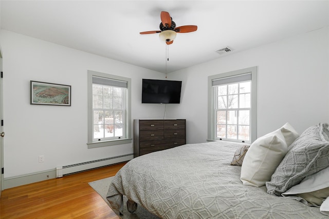 bedroom with wood finished floors, visible vents, baseboard heating, and multiple windows