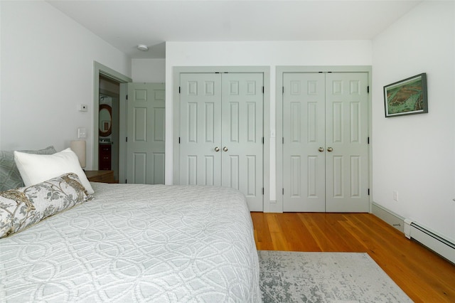 bedroom with a baseboard heating unit, wood finished floors, and multiple closets