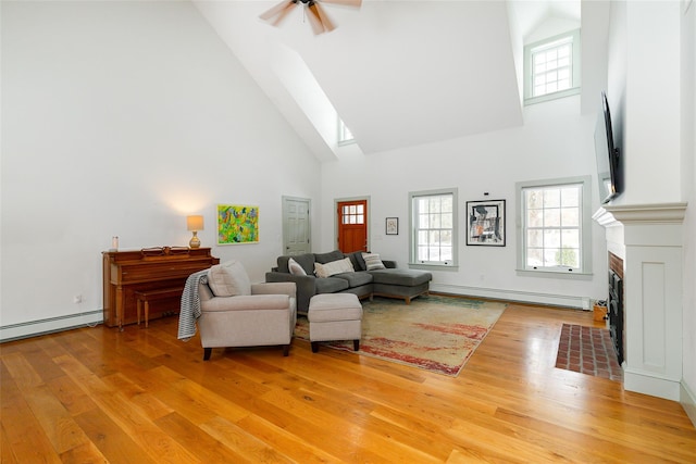 living area with light wood finished floors, baseboard heating, a high ceiling, a fireplace with flush hearth, and a baseboard heating unit