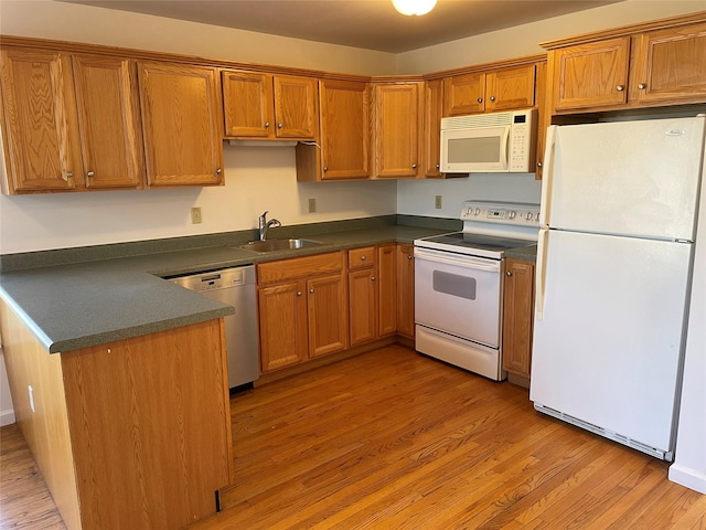 kitchen with dark countertops, white appliances, light wood-style floors, and a sink