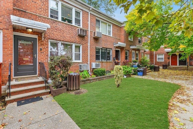 view of property featuring central AC, brick siding, a wall unit AC, and a front yard