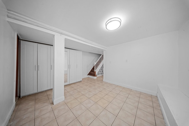 below grade area featuring light tile patterned flooring, baseboards, and stairs