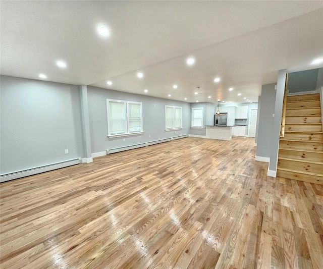 unfurnished living room featuring a baseboard heating unit, light wood-type flooring, recessed lighting, and stairs