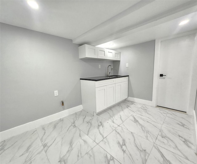 kitchen with a sink, white cabinets, baseboards, marble finish floor, and dark countertops