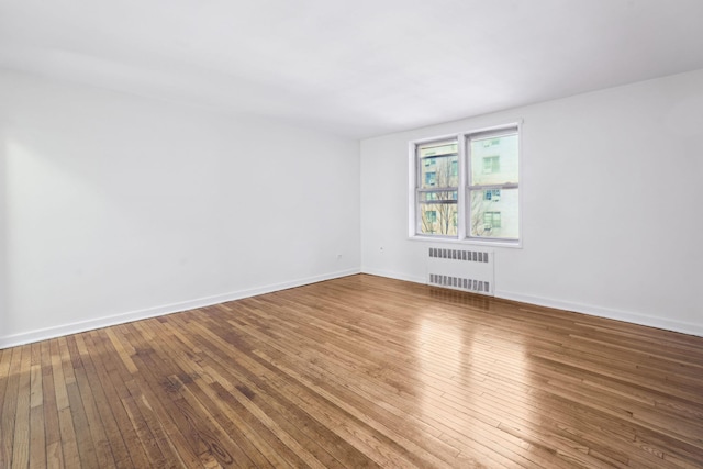 empty room featuring radiator, baseboards, and hardwood / wood-style floors