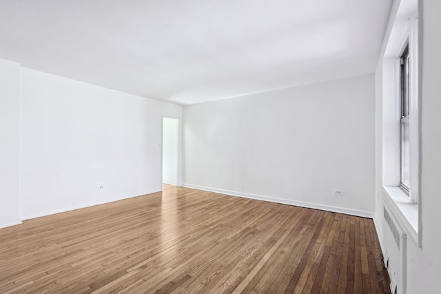 unfurnished room featuring wood-type flooring, baseboards, and radiator heating unit