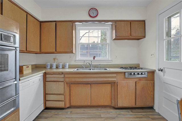 kitchen featuring white dishwasher, light countertops, light wood-type flooring, stainless steel oven, and a sink