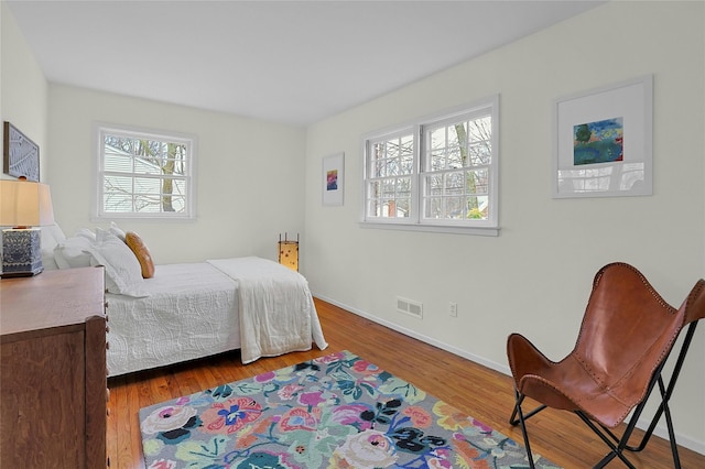 bedroom with wood finished floors, visible vents, and baseboards