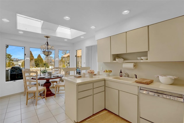 kitchen with a skylight, dishwasher, a peninsula, cream cabinets, and a sink