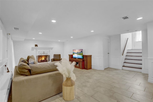 living room featuring stairway, a lit fireplace, visible vents, and a decorative wall