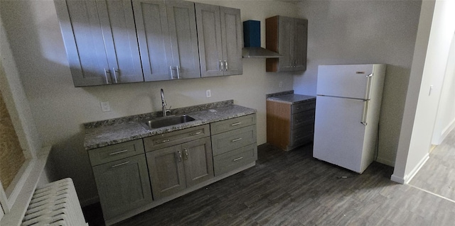 kitchen featuring dark wood-style flooring, radiator, freestanding refrigerator, a sink, and wall chimney exhaust hood