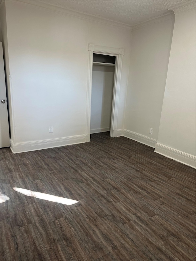 unfurnished bedroom with baseboards, ornamental molding, dark wood finished floors, and a closet