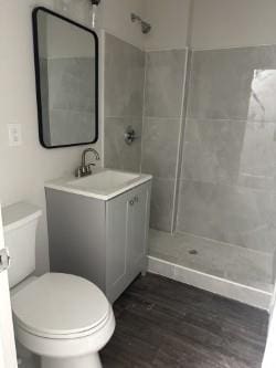 full bathroom with vanity, tiled shower, wood finished floors, and toilet