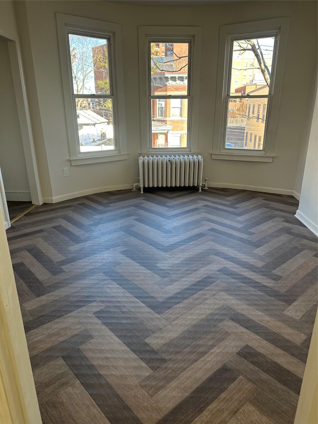 empty room featuring radiator heating unit, baseboards, and dark colored carpet