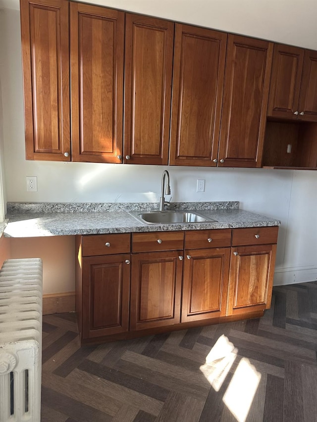 kitchen featuring brown cabinetry, baseboards, light countertops, and a sink