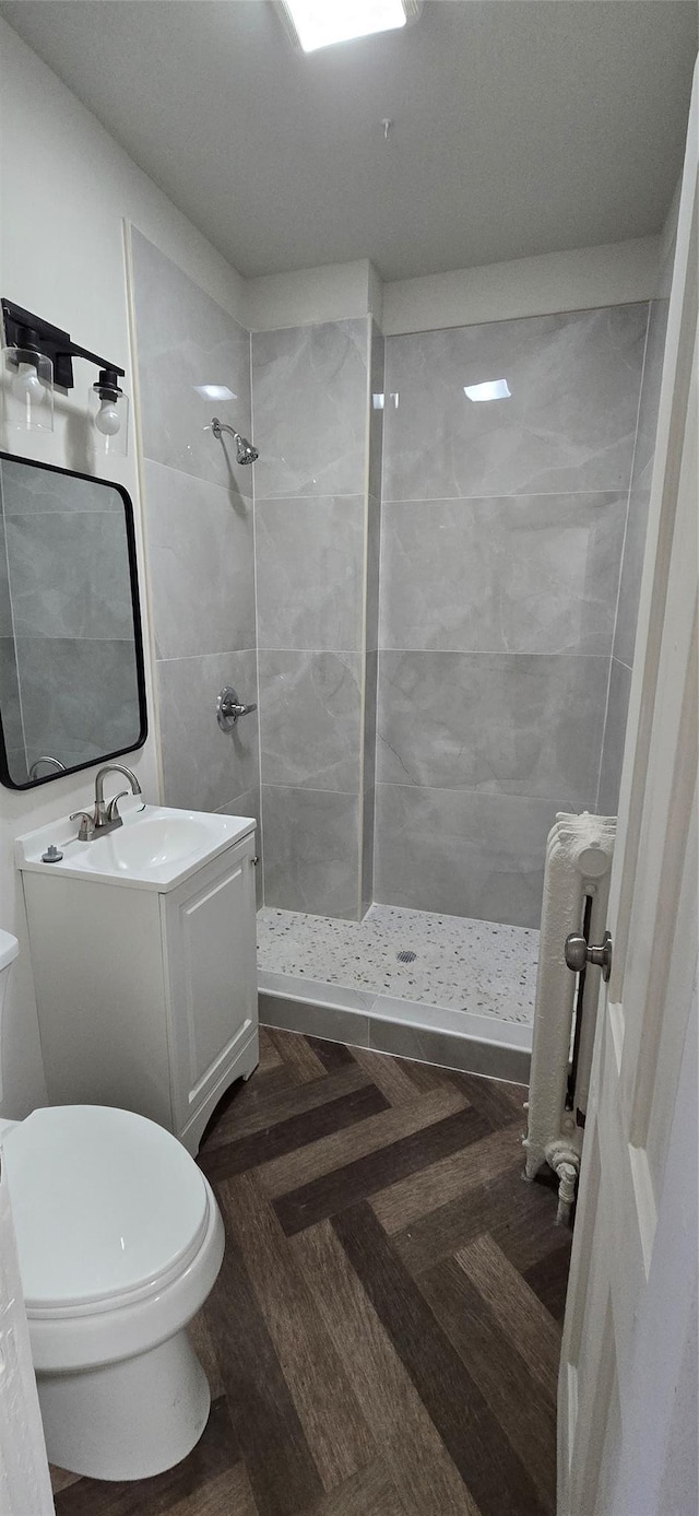 full bathroom featuring radiator, toilet, a tile shower, and vanity