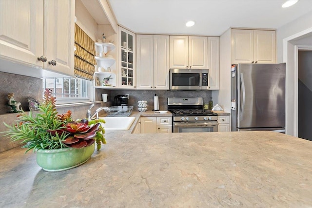 kitchen with stainless steel appliances, a sink, light countertops, tasteful backsplash, and glass insert cabinets