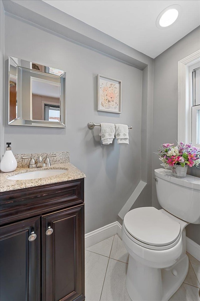 half bath with tile patterned flooring, baseboards, vanity, and toilet