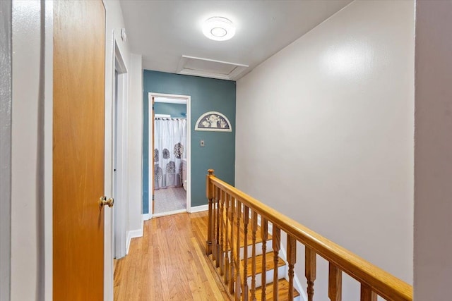 hallway featuring light wood-style floors, attic access, baseboards, and an upstairs landing