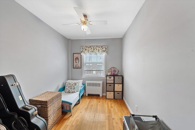 sitting room with baseboards, light wood-style floors, a ceiling fan, and radiator