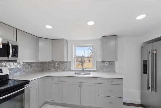 kitchen featuring light countertops, appliances with stainless steel finishes, a sink, and gray cabinetry