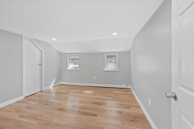 empty room featuring a baseboard heating unit, baseboards, lofted ceiling, and light wood-style floors