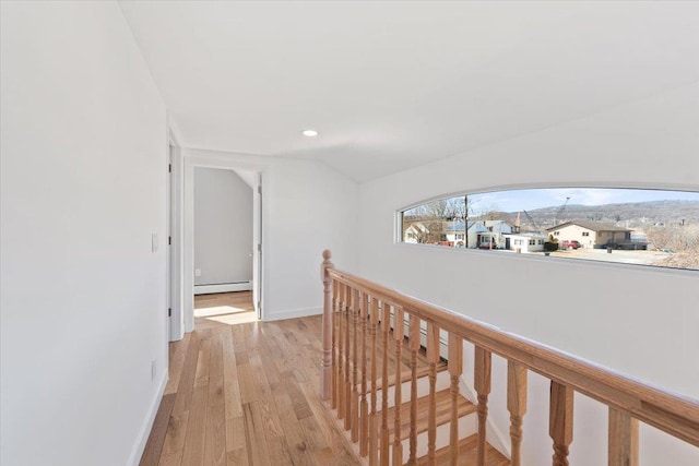 hall featuring light wood finished floors, lofted ceiling, a baseboard heating unit, an upstairs landing, and baseboards