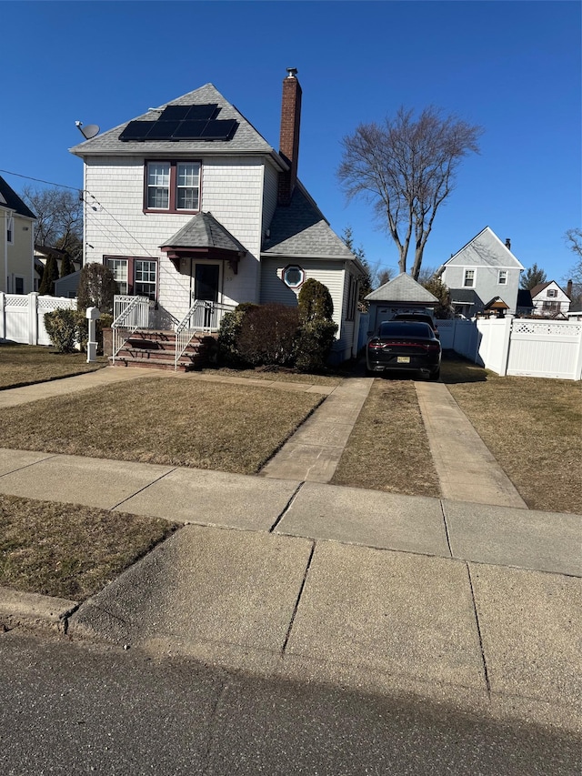 view of front facade with solar panels, fence, driveway, and a chimney