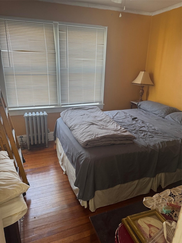 bedroom featuring radiator, hardwood / wood-style floors, multiple windows, and crown molding